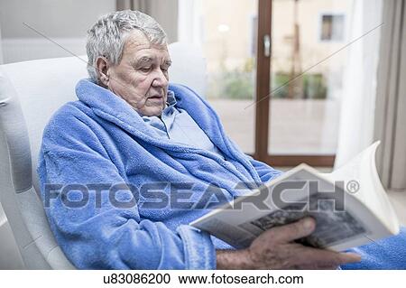 Stock Image - Senior man reading magazine in care home.. Fotosearch