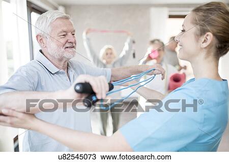 Stock Image - Senior man using resistance band in exercise class with physiotherapist.. Fotosearch