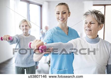 Stock Photograph - Senior woman holding hand weight, physiotherapist helping.. Fotosearch