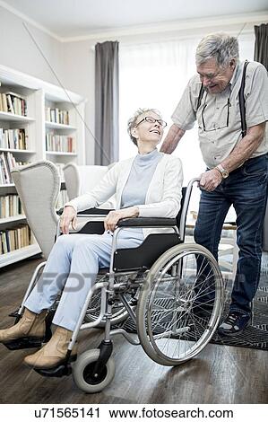 Stock Image - Senior woman in wheelchair looking at man and smiling.. Fotosearch