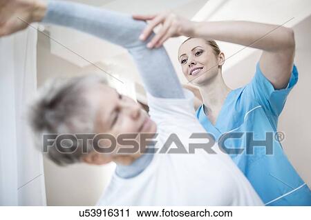 Stock Image - Senior woman stretching, physiotherapist helping.. Fotosearch