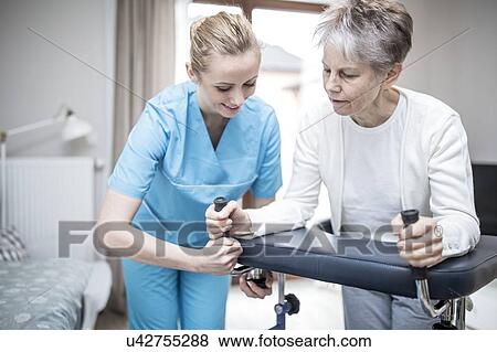 Stock Photo - Senior woman using rollator with care worker assisting.. Fotosearch