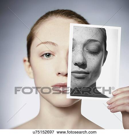 Stock Photo - Sun damage. Woman holding a photograph in front of her face showing the damage sun exposure has done to her skin.. Fotosearch