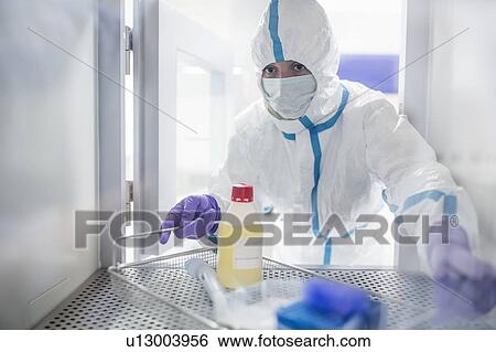 Stock Photograph - Technician collecting equipment from a transfer hatch in a sterile laboratory that manufactures human tissues for implants. Such implants include bone and skin grafts.. Fotosearch