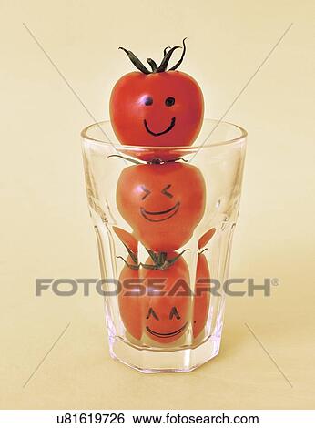 Stock Photograph - Three tomatoes with eyes and mouths drawn in black ink in a glass.. Fotosearch