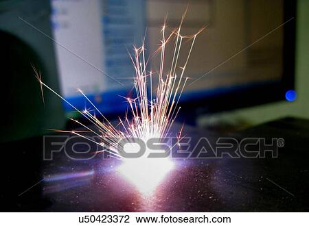 Stock Image - Titanium laser ablation. Spark from a laser being used to ablate a piece of titanium to form microstructures and nanostructures on the surface. This research involves the use of lasers to etch and ablate metal and semiconductor surfaces. The resulting.... Fotosearch