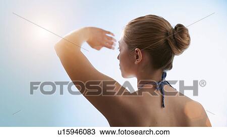 Stock Image - Woman shielding her eyes from the sun.. Fotosearch