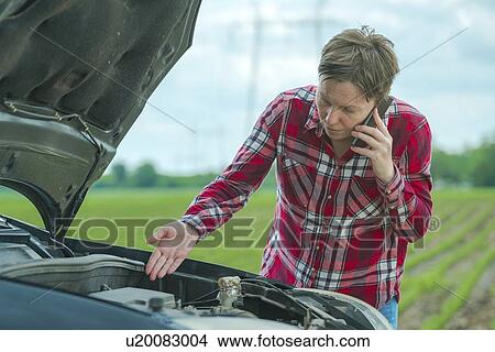 Picture - Woman standing by her broken down car on a country road and talking on her mobile phone.. Fotosearch