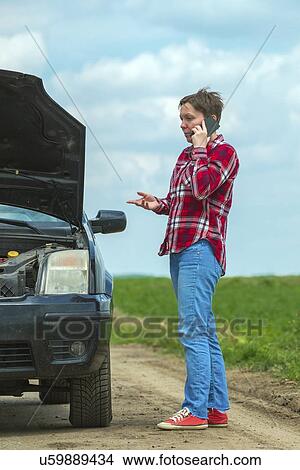 Woman standing by her broken down car on a country road and talking on her mobile phone. View Large Photo Image Picture - Woman standing by her broken down car on a country road and talking on her mobile phone.. Fotosearch