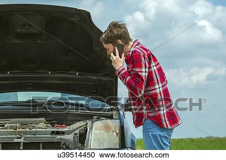 Stock Image - Woman standing by her broken down car on a country road and talking on her mobile phone.. Fotosearch