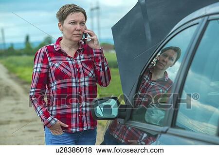 Stock Photo - Woman standing by her broken down car on a country road and talking on her mobile phone.. Fotosearch
