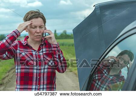 Stock Photo - Woman standing by her broken down car on a country road and talking on her mobile phone.. Fotosearch