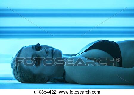 Stock Image - Woman wearing protective goggles in tanning booth.. Fotosearch