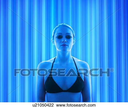 Stock Image - Woman wearing protective goggles in tanning booth.. Fotosearch