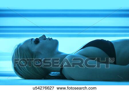 Stock Photo - Woman wearing protective goggles in tanning booth.. Fotosearch