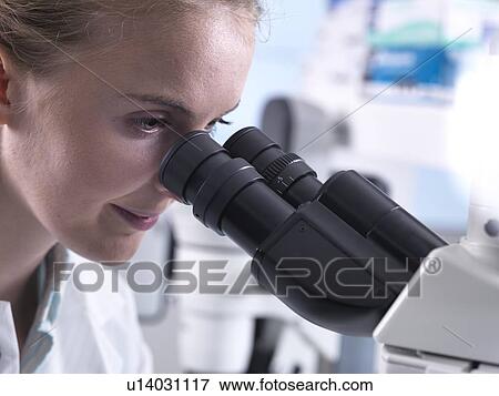 Stock Photo - Young female graduate viewing a sample down a microscope.. Fotosearch