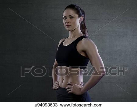 Stock Image - Young woman in sports top with hands on hips, portrait.. Fotosearch