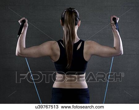 Stock Image - Young woman in sports top with resistance band, portrait.. Fotosearch