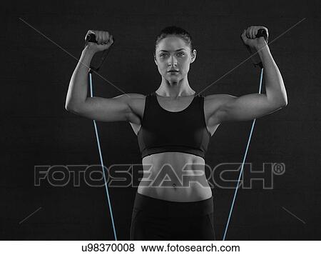 Stock Photo - Young woman in sports top with resistance band, portrait.. Fotosearch