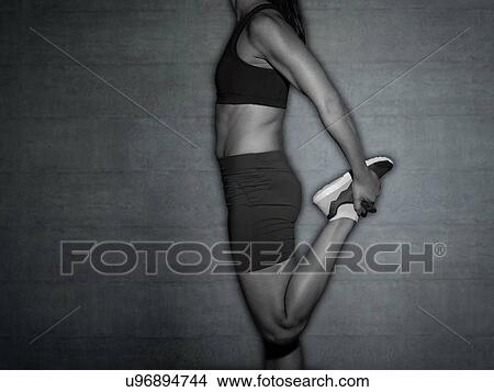 Picture - Young woman stretching leg, cropped shot.. Fotosearch