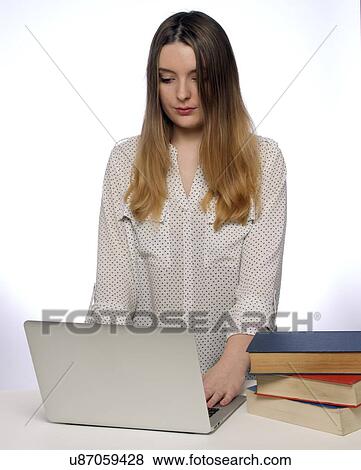 Stock Photo - Young woman using laptop with books.. Fotosearch