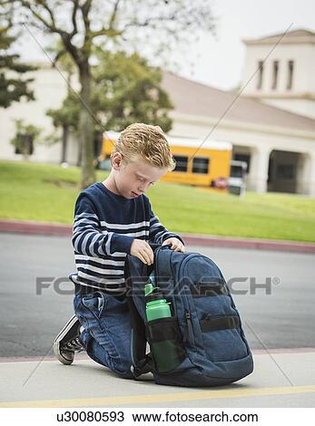 Stock Image - Boy kneeling by backpack. Fotosearch