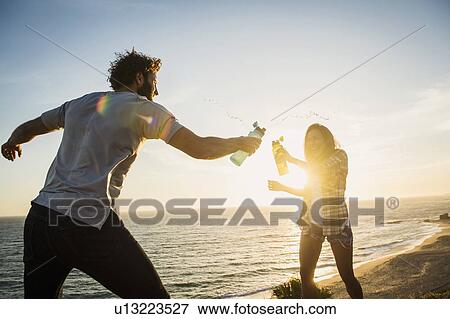 Couple having water fight on beach at sunset View Large Photo Image Stock Photo - Couple having water fight on beach at sunset. Fotosearch