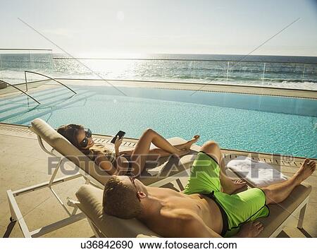 Couple relaxing by swimming pool by ocean View Large Photo Image Stock Image - Couple relaxing by swimming pool by ocean. Fotosearch