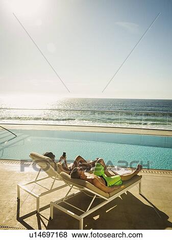 Stock Photo - Couple relaxing by swimming pool by ocean. Fotosearch