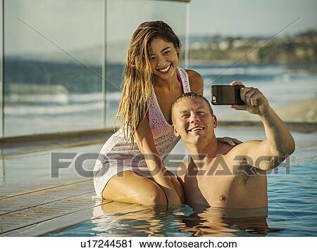 Stock Image - Couple taking selfie in swimming pool. Fotosearch