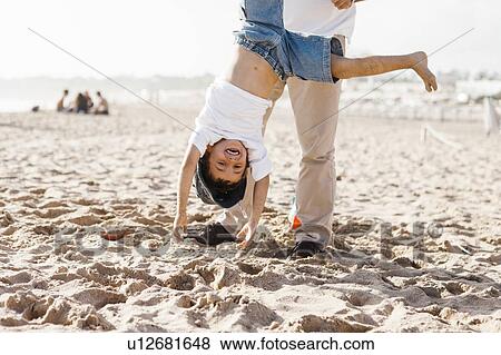 Stock Photo - Father holding son (4-5) upside down beach. Fotosearch