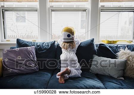 Stock Photo - Girl wearing helmet on sofa by window. Fotosearch