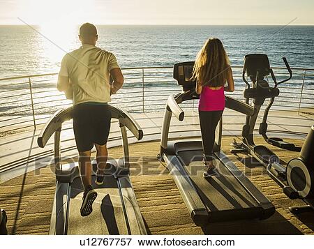 Stock Photo - Man and woman exercising on patio over sea. Fotosearch
