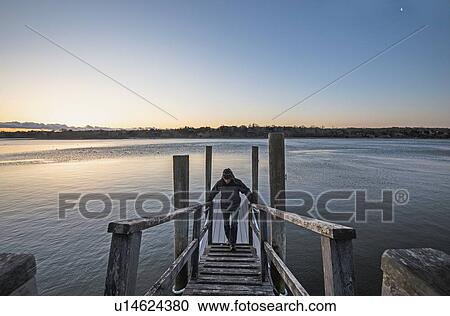 Man standing on pier at dawn View Large Photo Image Stock Image - Man standing on pier at dawn. Fotosearch