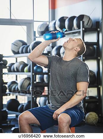 Stock Image - Mid adult man drinking in gym. Fotosearch
