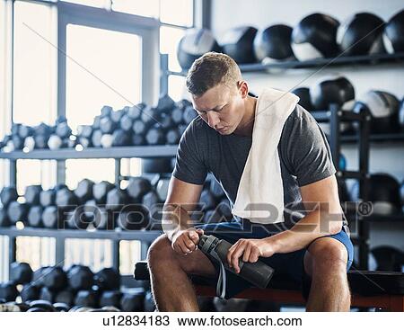 Stock Image - Mid adult man with towel and bottle in gym. Fotosearch