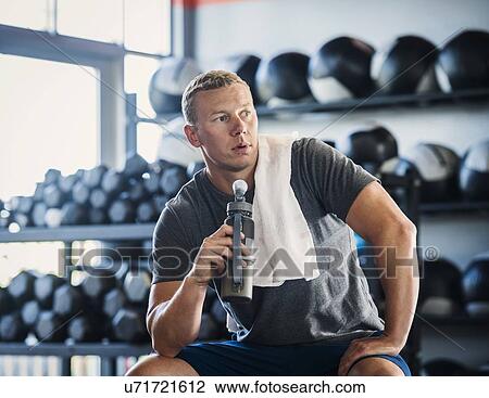 Stock Image - Mid adult man with towel and bottle in gym. Fotosearch