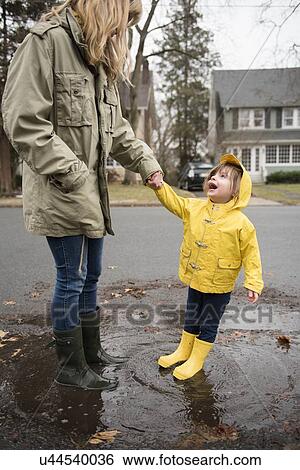 Stock Photograph - Mother and daughter (2-3) in puddle. Fotosearch