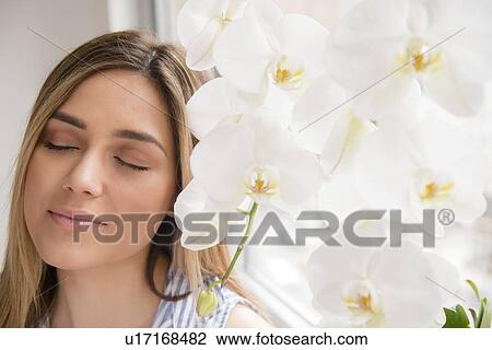 Stock Image - Portrait of young woman with closed eyes next to white orchid flowers. Fotosearch