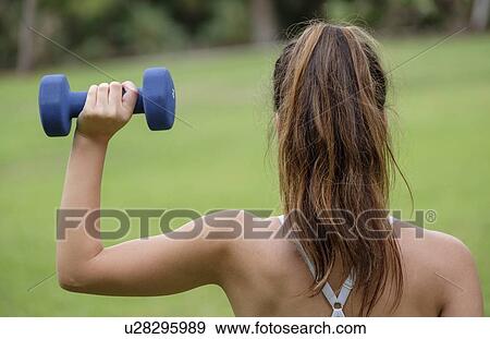 Stock Photo - Rear view of woman lifting dumbbell. Fotosearch
