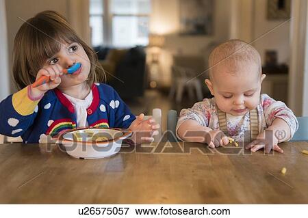 Stock Photo - Sisters (12-17 months, 2-3) having lunch at home. Fotosearch