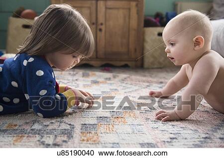 Stock Image - Sisters (12-17 months, 2-3) playing on carpet. Fotosearch