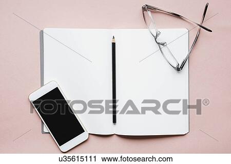 Stock Image - Smart phone, pencil and glasses on open notebook. Fotosearch