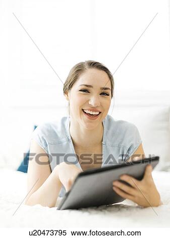 Stock Photography - Smiling woman holding folder on bed. Fotosearch