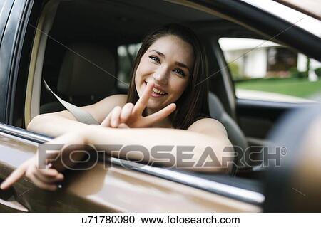 Smiling young woman doing peace sign in car View Large Photo Image Stock Image - Smiling young woman doing peace sign in car. Fotosearch