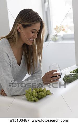Smiling young woman in kitchen, holding glass of red wine View Large Photo Image Stock Photo - Smiling young woman in kitchen, holding glass of red wine. Fotosearch