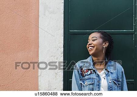 Stock Photo - Smiling young woman leaning against building. Fotosearch