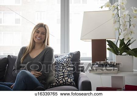 Stock Photography - Smiling young woman sitting on sofa. Fotosearch