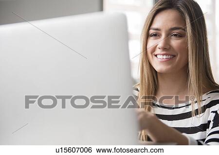 Stock Photograph - Smiling young woman using laptop. Fotosearch