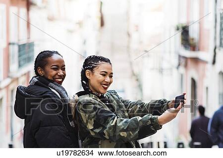 Picture - Two young women taking selfie outdoors. Fotosearch